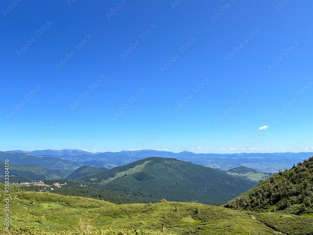 Naklejka premium Scenic mountain landscape with green hills and vibrant blue sky.