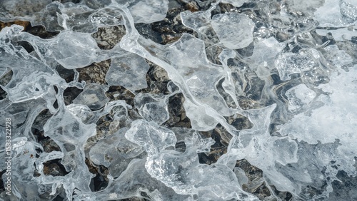 Macro shot of clear ice structures with smooth curves and half-buried pebbles in a melting river environment. The artistry of nature's unpredictable charm.