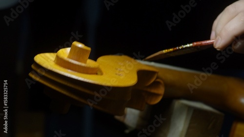 Obraz na plátně Luthier working on a cello scroll, applying varnish with a brush in a dimly lit