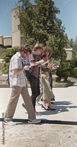 Wallpaper Mural Diverse university students walks across a campus path, deeply engrossed in their tablets and notebooks. They are actively engaged in learning and collaborative study, showcasing modern education. Torontodigital.ca