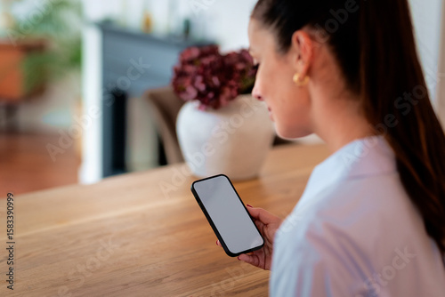 Close-up of a woman sitting at a table and using a blank screen smart phone
