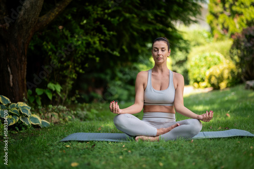 Attractive woman wearing sports clothes and doing yoga in the garden at home