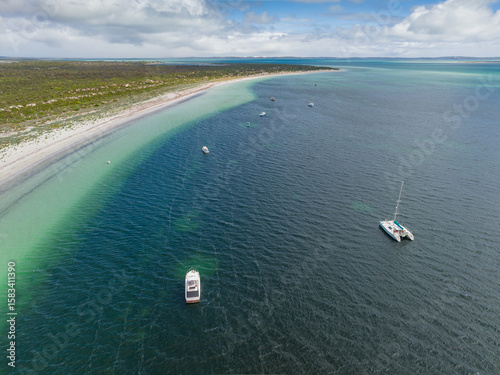 Aerial view of boats on a blue sea scattered along a remote coastline