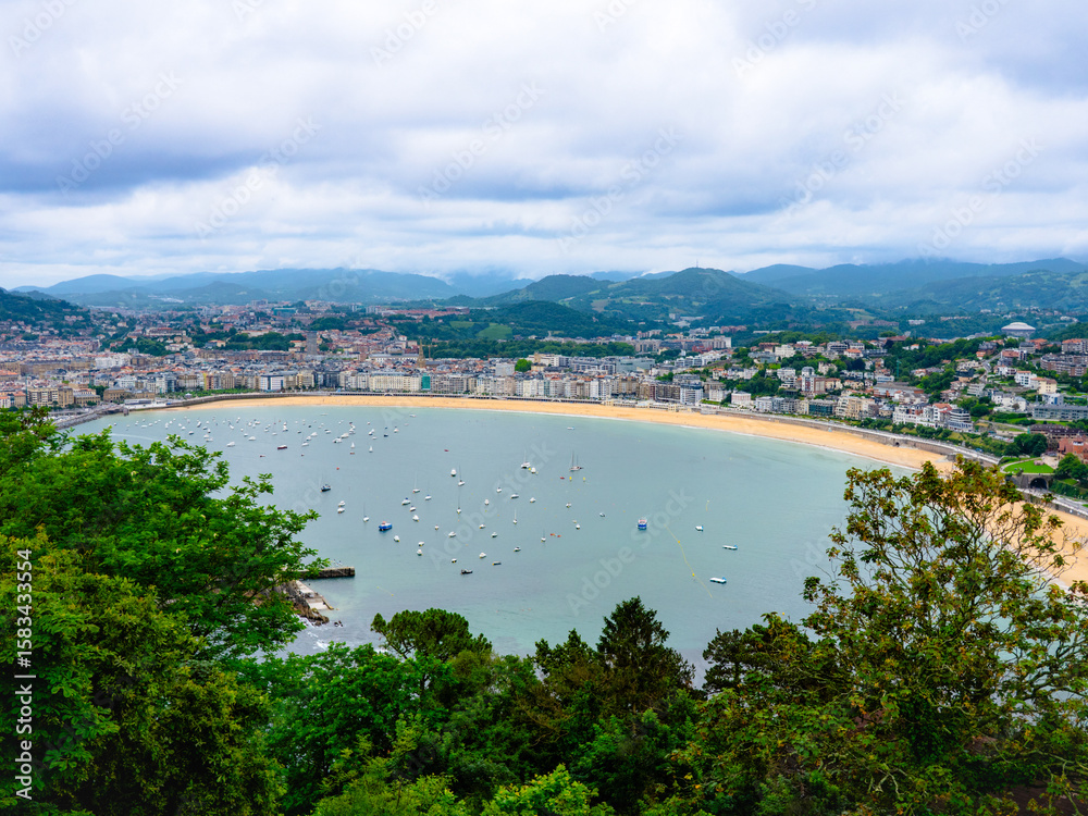 Fototapeta premium La Concha Bay in San Sebastián, Spain, viewed from Mount Igueldo—panoramic coastal scenery with sandy beach, boats, and cityscape under a dramatic sky, perfect for travel and vacation imagery.