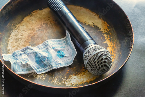 Microphone and dollar bill on a dirty old frying pan close-up, journalistic ethics, fake news, fact manipulation, yellow press, bribery of journalists.