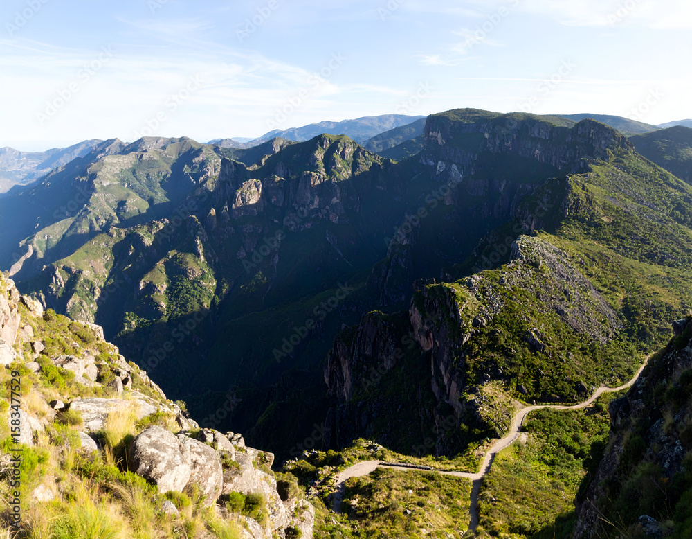 Fototapeta premium Expansive mountain landscape with dramatic shadows and a winding road through the wilderness.