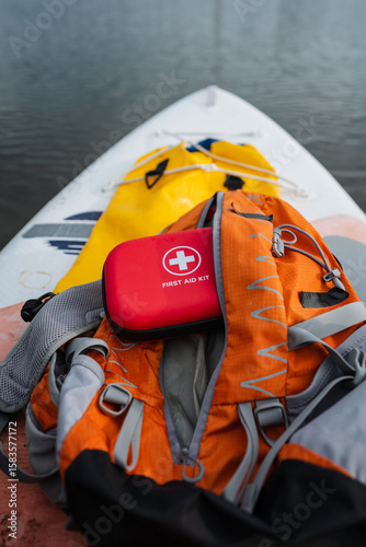 A wellequipped first aid kit is positioned conveniently on top of an orangecolored backpack that is resting on a paddle board, ready for any possible adventure or emergency