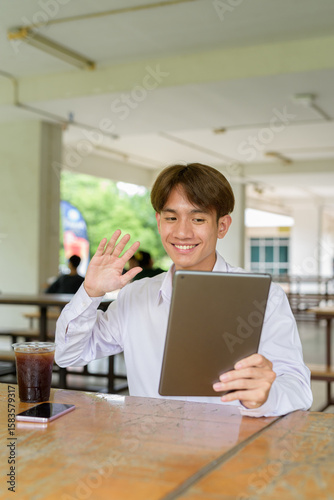 Non binary university student sitting in college campus using tablet computer