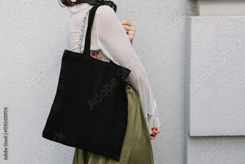 Young white woman holding black eco bag on arm shoulder or hand, street wall at background. city living female going on shopping to grocery store