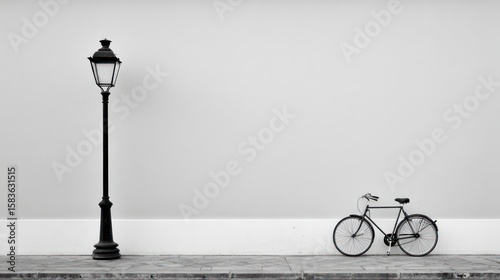 A grayscale image of a lamppost and bicycle against a white wall