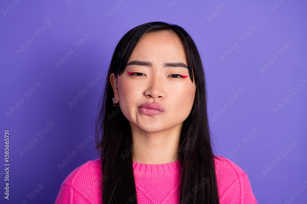 Fototapeta premium Young multiethnic woman in pink sweater against purple background displaying pensive and comical expression folding lips