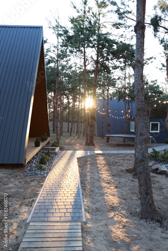 Modern A-frame cabin in a pine forest with hammock, trampoline, and string lights. Peaceful woodland retreat with cozy outdoor vibes