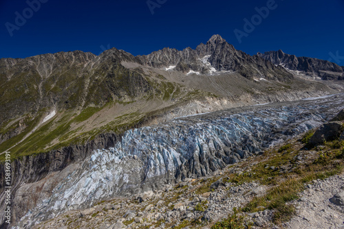 Beautiful mountain landscapes of the Alps on Tour du Montblanc hike. Green valley, snow summits and rocky peaks of Aiguilles de Chamonix and Montblanc. Summer sunny weather blue sky, trekking Alp hike