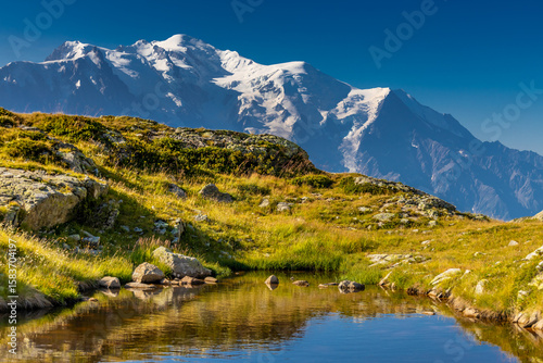 Beautiful mountain landscapes of the Alps on Tour du Montblanc hike. Green valley, snow summits and rocky peaks of Aiguilles de Chamonix and Montblanc. Summer sunny weather blue sky, trekking Alp hike
