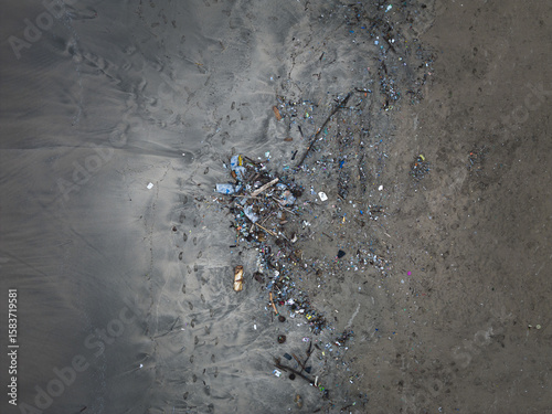 Aerial view of discarded trash and debris scattered on a sandy beach, contrasting with the natural landscape, Badung, Bali, Indonesia.