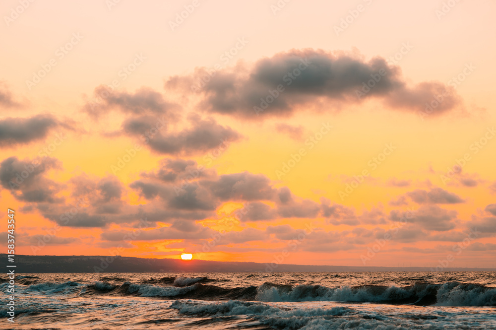 Fototapeta premium A stunning sunset over sparkling ocean waves, adorned with vibrant colors and soft clouds, creating a serene scene
