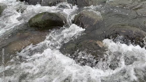 Fast flowing mountain river water flows over through the stones. A very clear mountain river, with fast and powerful river waves flowing between the rocks. Splash river water. Beautiful lansdscape.