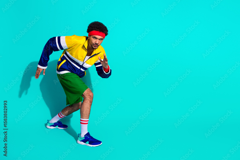 Naklejka premium Retro styled young male athlete in vibrant activewear striking a dynamic pose against a teal background representing sports fashion