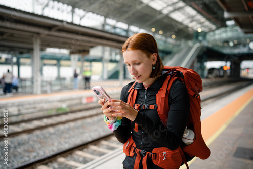 Backpacker using smartphone at train station while waiting for train