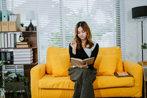 Fotografie Attractive young asian woman leaning of sofa, reading a novel book