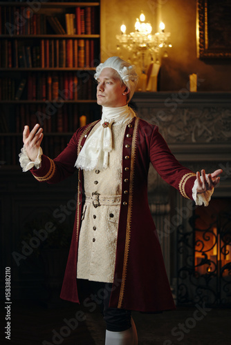Caucasian middle aged man wearing historical Baroque costume standing with arms raised in elegant gesture in ornate library setting, embodying Renaissance period fashion and style
