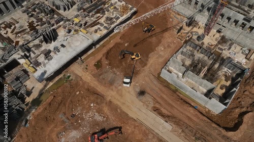 An excavator loads a dump truck with sand at a construction site, shot from drone