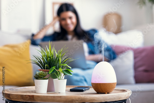 Photos Essential oil aroma diffuser humidifier the air while woman working with laptop sitting on coach