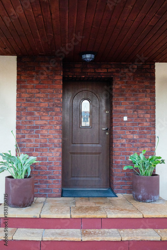 Inviting front entrance with a grand wooden door, stone accents, and decorative plants displayed. Facade of a modern building with modern doors. Designer entrance door to country house. Modern design.