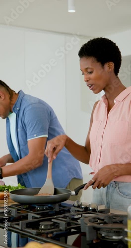 Vertical video: Diverse couple warming frying pan on gas stove, chopping tomatoes and stirring food