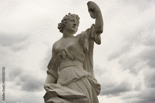 A beautiful marble statue of Melpomene, the ancient Greek muse of tragedy, holds a tragic mask before a dramatic cloudy sky