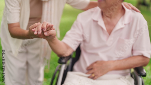 Принти на полотні Asian senior couple support healthcare holding hands wheelchair park garden elde