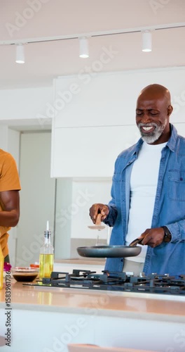 Vertical video: African American father and son pressing spatula on pan, son plating meal at island