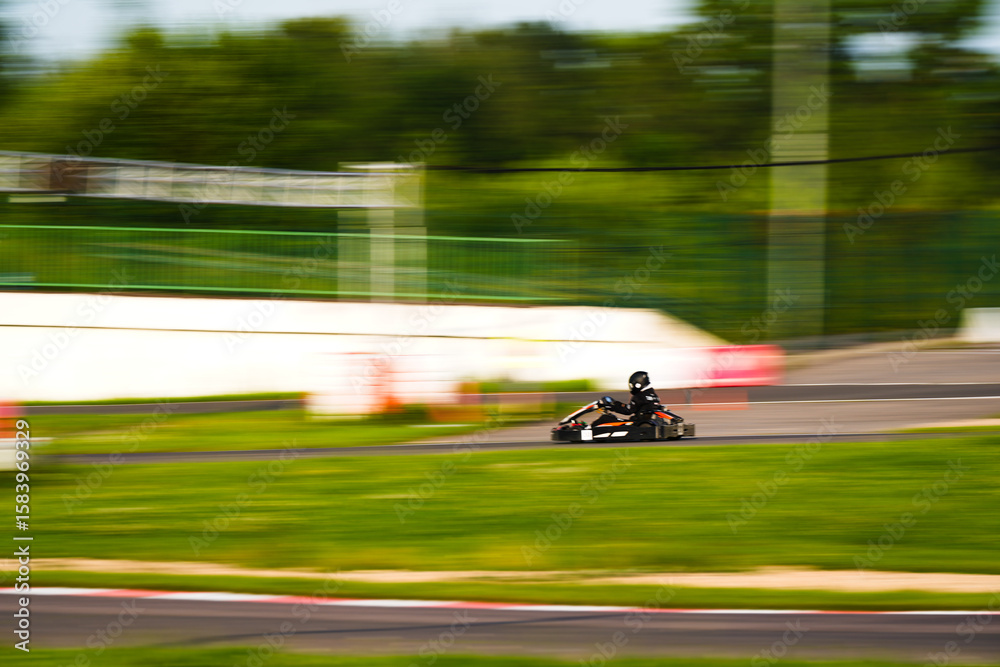 Obraz premium Dynamic photo of a go-kart racer speeding along a track. The motion blur effect emphasizes velocity, action, and the thrill of motorsport. Suitable for themes of competition, adrenaline, racing