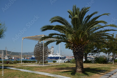 Neatly trimmed palm trees grow on lawns near the seaport in the city of Volos, Greece