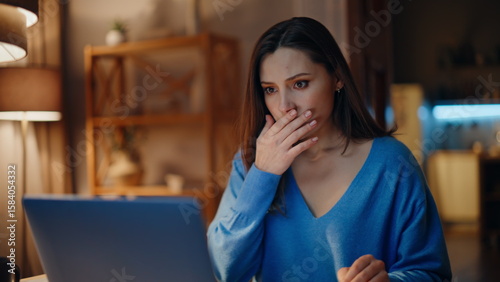 Concerned brunette reading email at laptop in dark home closeup. Desperate woman