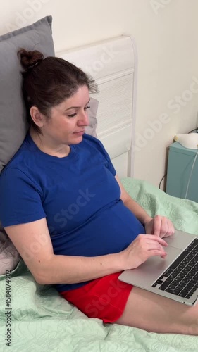 Caucasian woman sitting on bed typing on laptop. 