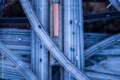 Aerial view of layered freeway overpasses in Los Angeles at twilight, with minimal traffic and graphic concrete lines forming a futuristic urban pattern