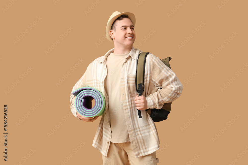 Fototapeta premium Young man with backpack and sleeping mat on brown background. Travel concept