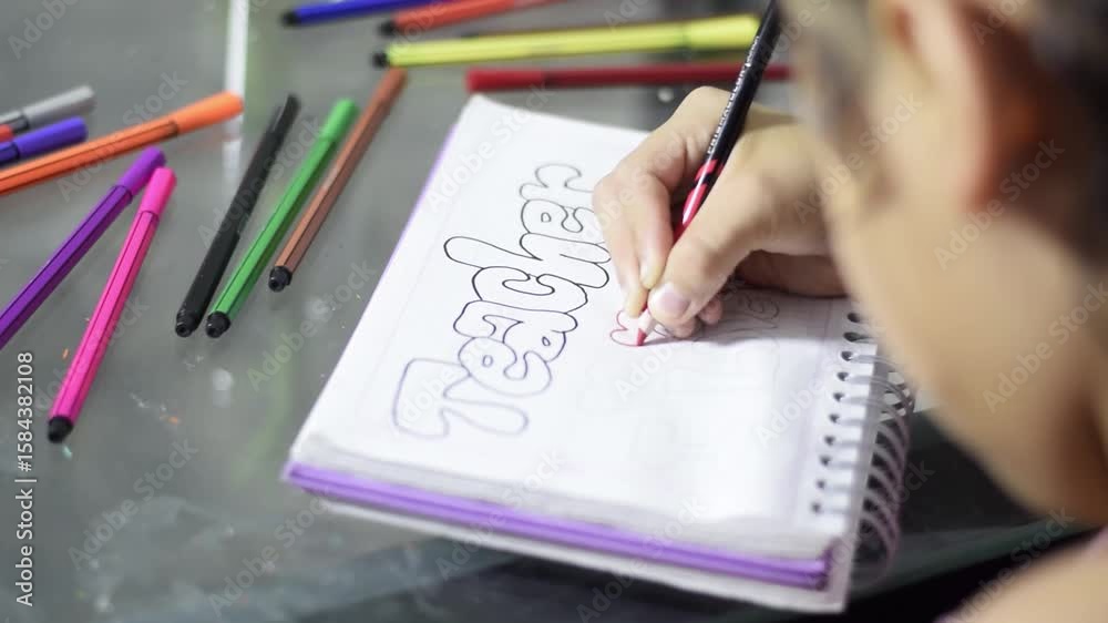 Girl outlining capital letters in red on a spiral notebook with a fine-point red pencil and colored pencils.