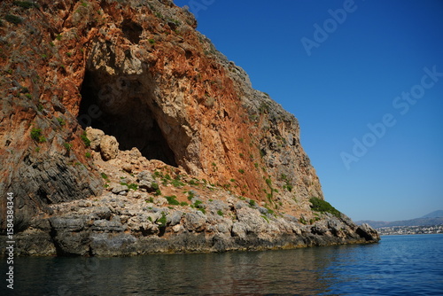 Majestic sea cave nestled in a rocky cliff by the ocean. Rugged geological formations and vibrant colors create a mesmerizing natural landscape. Tranquil sea and clear sky complete the scene.
