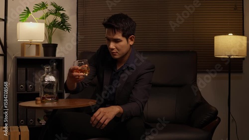 Asian businessman sitting and drinking whiskey in a room on a sofa.