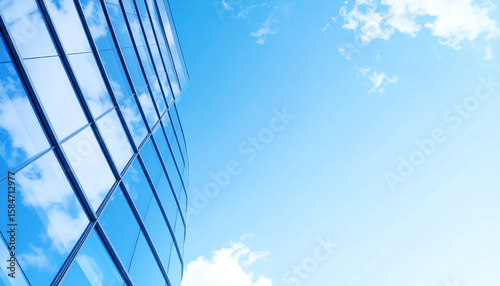 A modern glass building reflects the blue sky and clouds, showcasing sleek architecture and a bright, open atmosphere