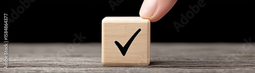 Checkmark wooden block held by fingers wooden surface with black
