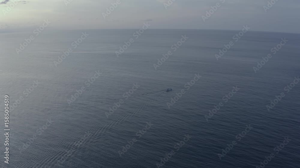 Aerial view of a small boat moving across calm ocean waters off the coast of Bali, Indonesia. Peaceful and cinematic drone shot captured at sunrise with a wide open horizon. Aerial view of a small boat moving across calm ocean waters off the coast of Bali, Indonesia. Peaceful and cinematic drone shot captured at sunrise with a wide open horizon.
