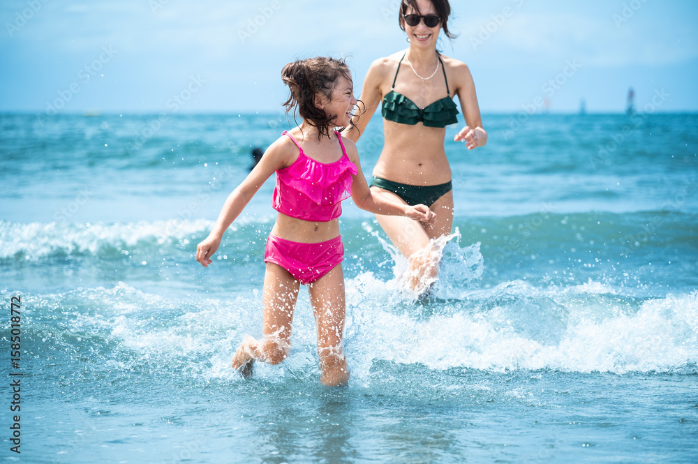 Happy mother and daughter laughing and running through sea water at Zushi beach Happy mother and daughter laughing and running through sea water at Zushi beach