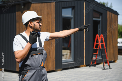 Obraz na plátně Construction worker directing modular house placement with walkie talkie