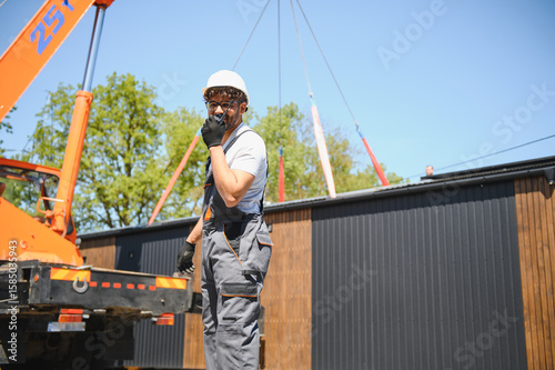 Construction worker supervising lifting of modular house onto truck