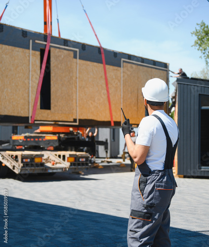 Tablou pe pânză Construction worker supervising loading of modular house onto truck