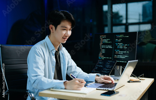 Young male programmer working with tablet and screen displaying code. Modern tech office setup, great for software