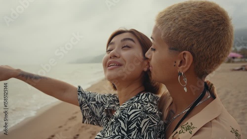 Passionate lesbian couple sharing tender moment while embracing and kissing on sandy beach during romantic sunset, expressing deep love and connection
